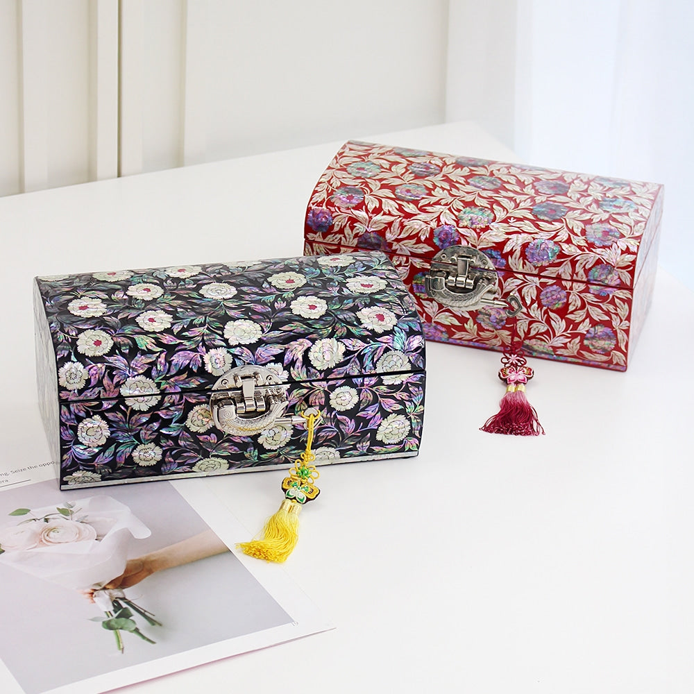 Two domed Korean jewelry boxes in black and red lacquer, open peony blossoms and leafy vines inlaid in mother-of-pearl across the lids and sides, silver clasps with silk tassels