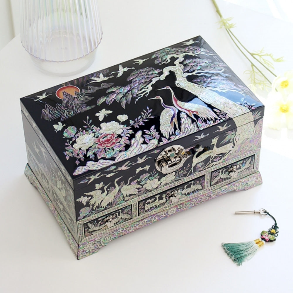 Black lacquer Korean jewelry box with a lidded top above a row of drawers, two cranes beneath a pine, a peony, deer and a red sun inlaid in mother-of-pearl
